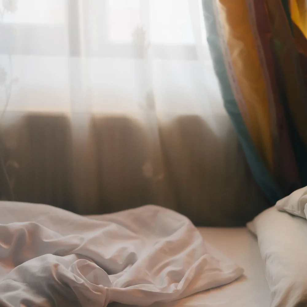 Morning light through a curtain falling across rumpled linen bedding.